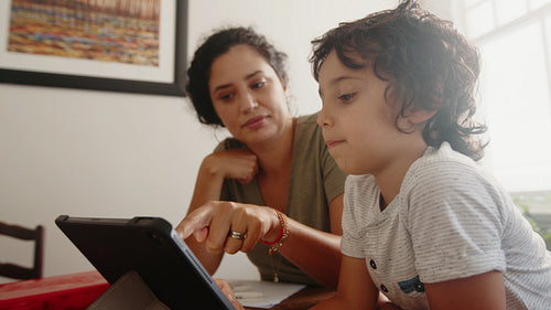 Homeschooling and distance learning: Mom teaching her son using a digital tablet at home
