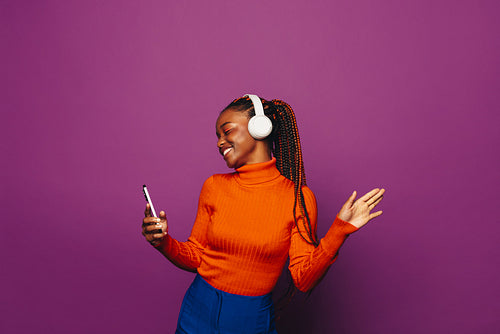 Happy girl dancing and holding a smartphone with vibrant purple background