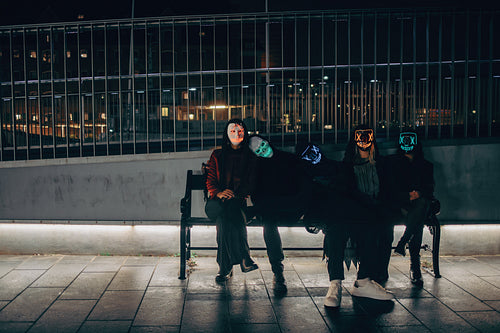 Friends relaxing on a city bench after a Halloween party at night