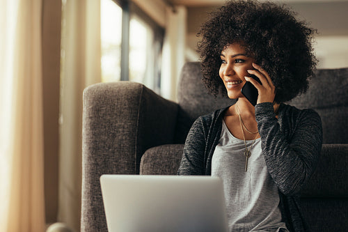 Beautiful woman at home with laptop and talking on cell phone