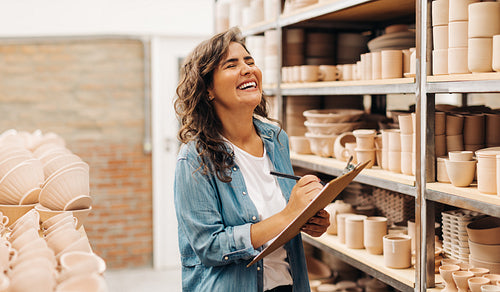 Cheerful young ceramist laughing happily in her shop
