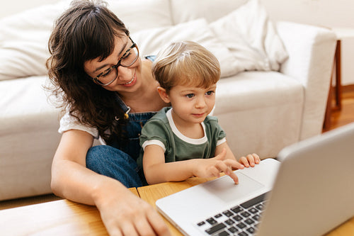 Small boy learning using laptop with mom