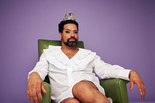 Confident drag queen sitting on arm chair