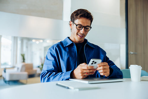 Man in blue jacket using smartphone at desk