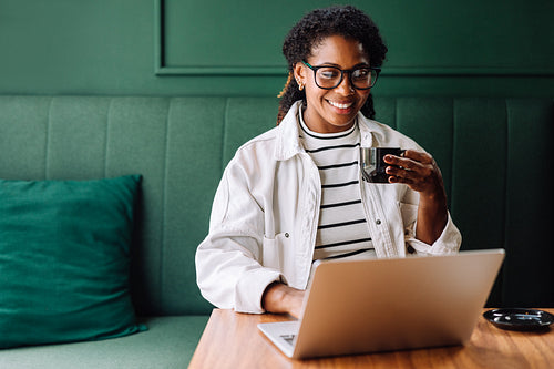 Smiling black woman enjoying coffee while using laptop