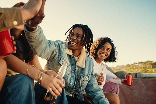 Happy young friends enjoying outdoor gathering with drinks and laughter