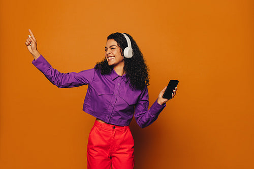 Vibrant woman celebrating to music with cheerful moves and a bright orange background
