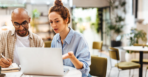 Two business people using a laptop as they work on a project in a cafe