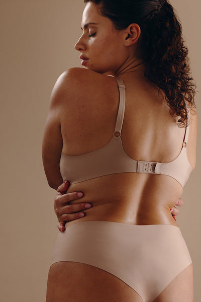 Woman in nude underwear embracing her own curvy body