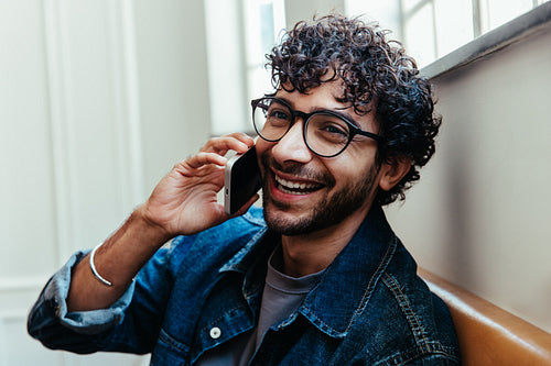 Stylish man with curly hair and glasses having a happy phone call during a business meeting