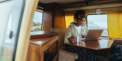 Balancing work and travel: Woman using laptop with a warm drink inside a camper van