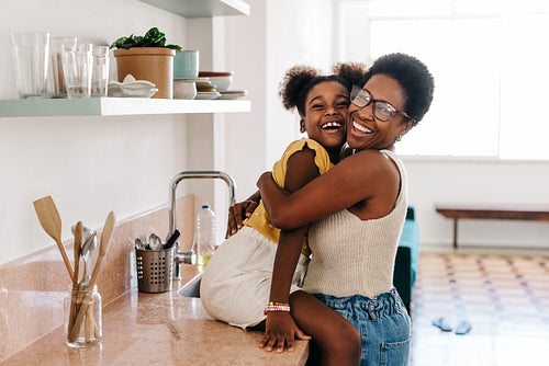 Mama's love: Happy black mom hugging her daughter in the kitchen