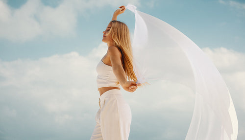 Young woman in white dancing freely under a bright sky