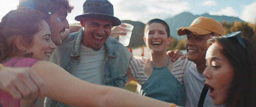 Young friends embracing, laughing and drinking beer at music festival