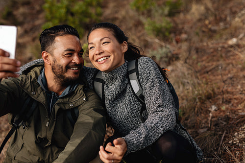 Couple sitting on mountain trail taking selfie
