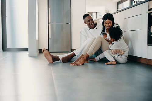 Family of three playing together and having fun while sitting on the floor in the kitchen