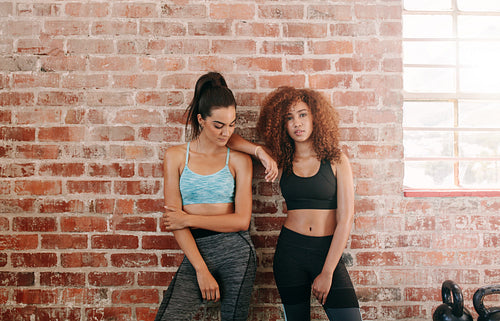 Young female friends standing against wall in gym