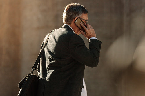 Senior man using mobile phone while walking on street to office