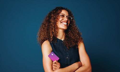 Confident woman stands with a banking card in a blue studio portrait