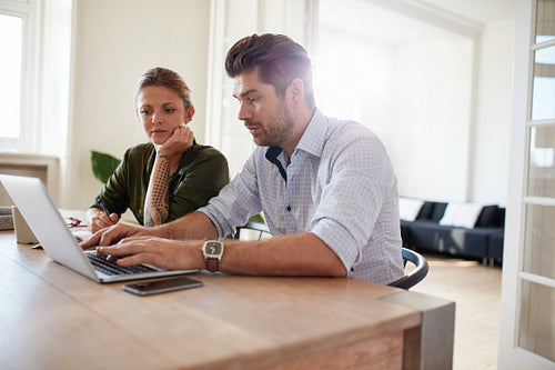 Young man working on laptop with woman sitting by