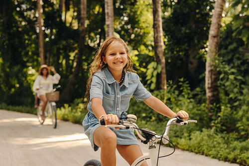 Happy girl biking at a resort during vacation with lush green background