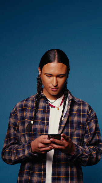 Young man smiles while looking at his phone against a blue backdrop
