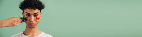 Gay man getting pride flag painted on his face