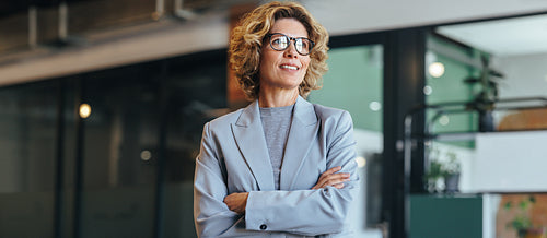 Thoughtful business woman standing with crossed arms. Woman in her 40's working in an office