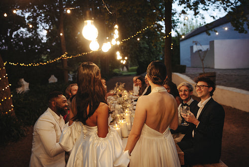 Two brides celebrating with guests at outdoor LGBTQ wedding dinner