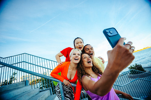 Taking photo, friends gather with a smartphone by the waterfront in sunny light