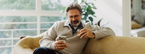 Senior man checks smartphone on sofa in home