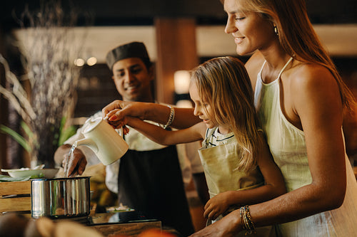Mother and child cooking together with a chef in a warm kitchen