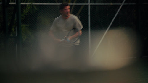 A determined male adult plays an intense game of tennis on a green outdoor court