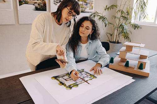 Two architects discussing draft plans with a cellphone in a creative space