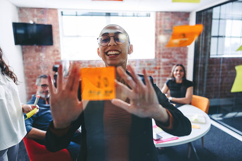 Smiling businesswoman sticking adhesive notes to a glass wall in