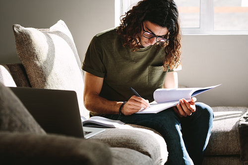 Male student writing notes sitting at home