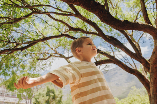 Happy child enjoys a sunny day under green trees outdoors