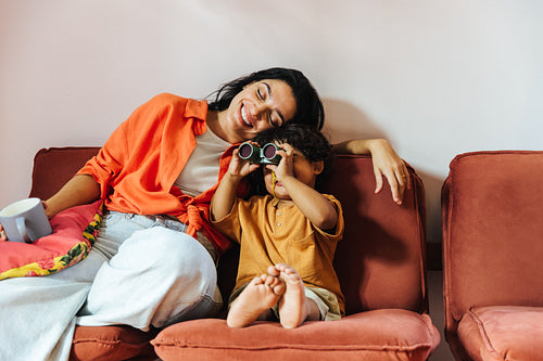 Mother and child spending time together with binoculars indoors on a sofa