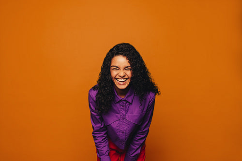 Cheerful woman with stylish curly hair standing against a vibrant orange background