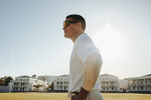 Male cricket player wearing sunglasses standing outdoors on a sunny day
