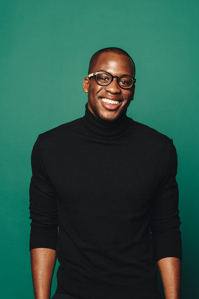 Confident young man with stylish glasses, smiling in casual attire on green background