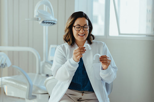 Her orthodontist expertise is reflected as the dentist holds a clear aligner in the clinic