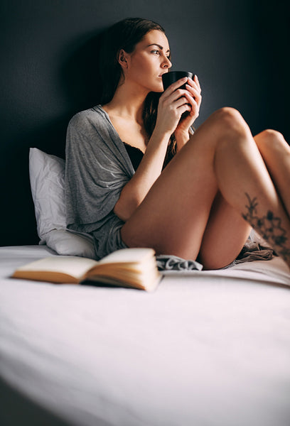 Young lady on bed drinking coffee looking away thinking