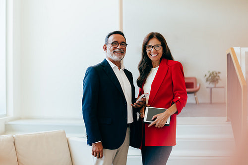 Senior executives smiling confidently with documents and devices in office environment