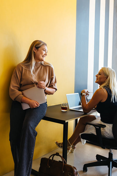 Two female colleagues discussing work in a brightly colored modern office setting