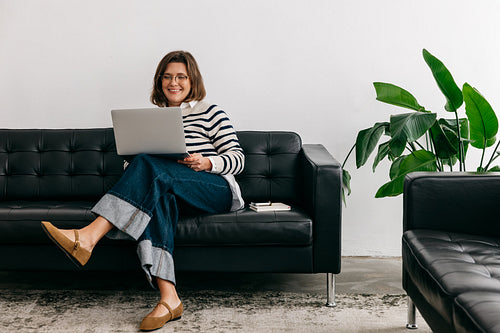 From home, the woman works on a couch with a laptop in the living room