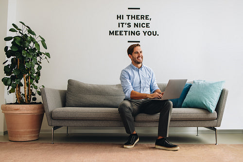 Confident businessman on sofa using laptop and looking away