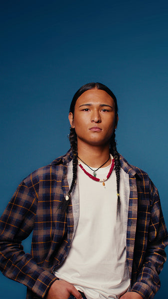 Confident young man with braids posing in a studio portrait against blue background