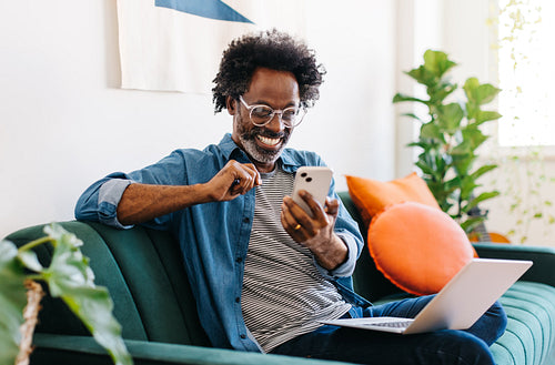 Afro mature man smiling and reading a text message on his smartphone at home