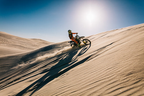 Motocross biker racing across sand dunes